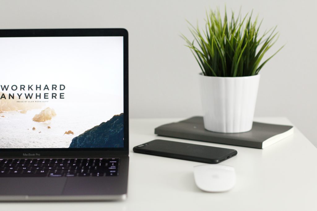 Open laptop with "work hard anywhere" image on screen sitting on a desk with a plant.