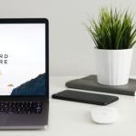 Open laptop with "work hard anywhere" image on screen sitting on a desk with a plant.